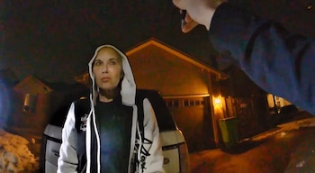 Kim Mathers, con chaqueta con capucha blanca y negra, es vista de noche desde una cámara corporal con una mano en la parte superior derecha