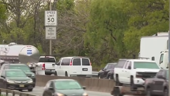 Vehículos moviéndose en una autopista de varios carriles, incluyendo un SUV blanco, una furgoneta blanca y un camión cisterna. Se ve una señal de límite de 50 mph