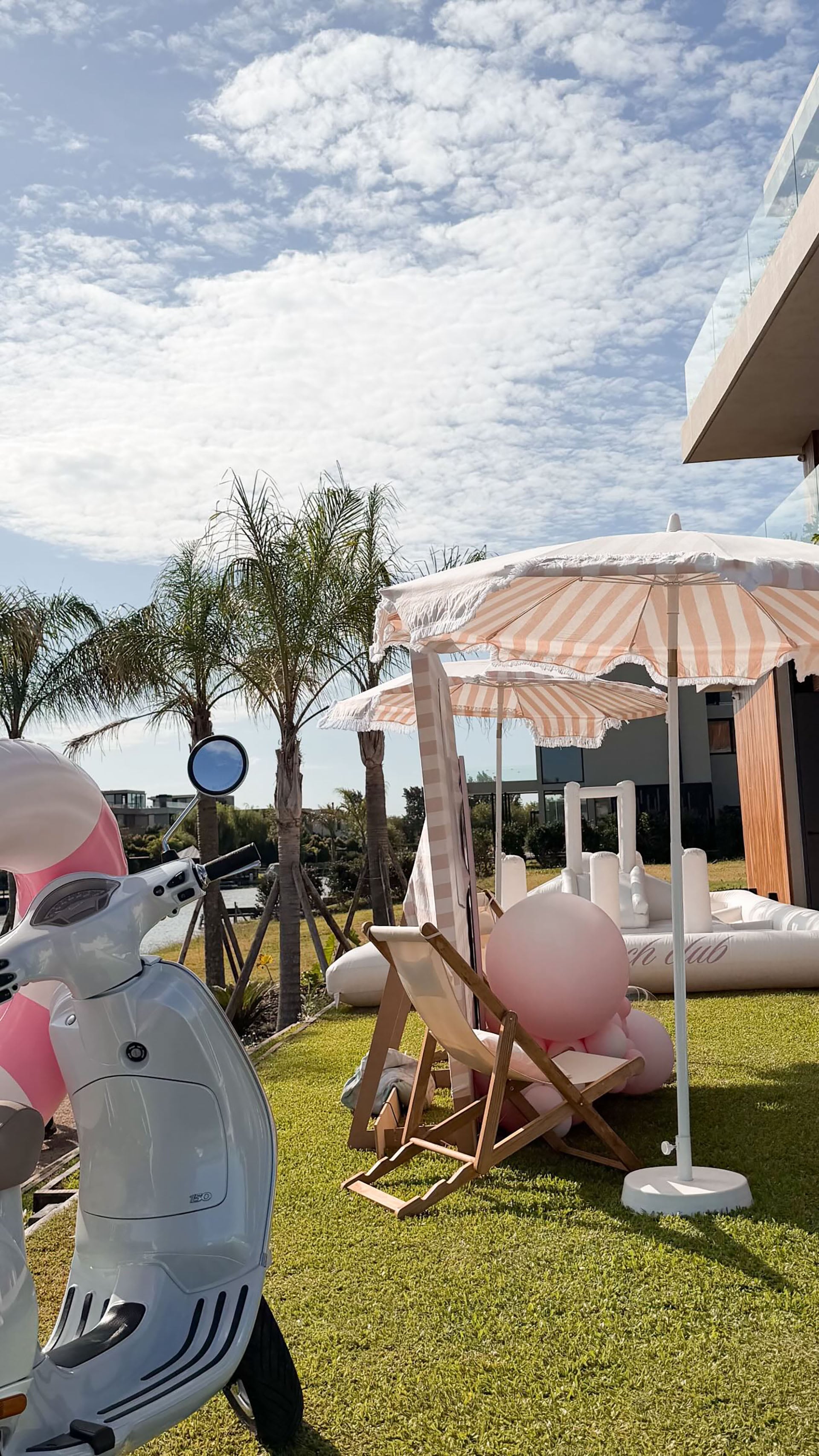 Reposeras de lona clara y sombrillas rayadas se distribuyen cerca de la casa, bajo palmeras y globos rosados (Instagram)