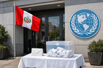 Fachada de edificio gris, bandera de Perú ondeando, logotipo azul redondo de globo terráqueo con ramas de olivo. Mesa con mantel blanco, sobre blanco, urna transparente con papeles.