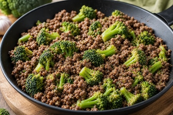 Sartén negra sobre una superficie de madera que contiene carne picada cocida y trozos de brócoli verde.