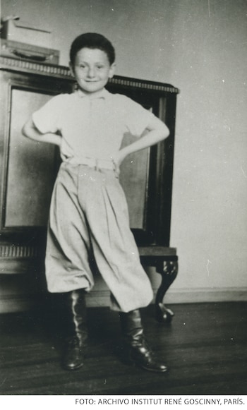 Fotografía en blanco y negro de un niño de pie con las manos en la cintura, camisa clara, pantalones holgados y botas altas