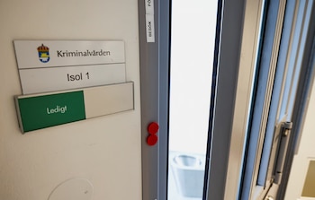 Primer plano de una puerta de metal gris en una instalación sueca con carteles blancos que leen 'Kriminalvården', 'Isol 1' y 'Ledigt' (Vacante)