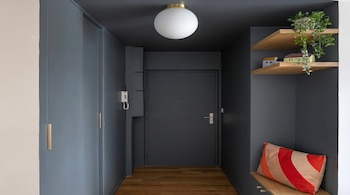 Pasillo moderno con paredes y puerta gris oscuro, suelo de madera, lámpara de techo esférica. Estantes con planta, mini casas y cojín a rayas.
