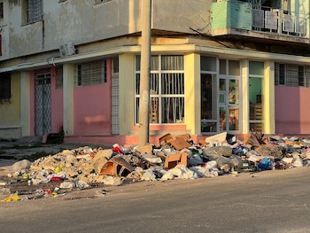 Un gran cúmulo de basura, incluyendo cajas, bolsas y escombros, yace en una calle frente a un edificio con paredes rosadas y amarillas en La Habana, Cuba