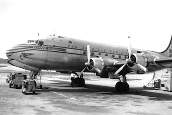 Avión Pan American World Airways Clipper Endeavor de cuatro hélices en tierra. Se observan equipos de asistencia en pista y personal