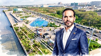 Ilustración acuarela de un hombre con traje oscuro y camisa blanca, la bandera de Colombia en la solapa, sobre un fondo urbano con río, parque, autos y edificios.