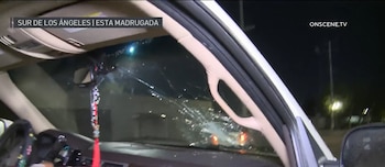 Vista desde el interior de un coche mostrando un parabrisas severamente agrietado, con un espejo retrovisor y un adorno colgando, de noche