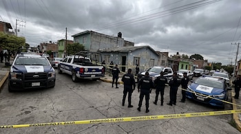 Calle con patrullas de Policía de Investigación y Policía Morelia, agentes policiales, cinta amarilla de seguridad y fachada de una vivienda en Morelia.