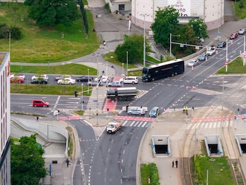 Vista aérea de un cruce urbano con vehículos, autobús, camión, furgoneta, vehículos policiales, vías de tranvía, túneles, edificios, árboles y personas
