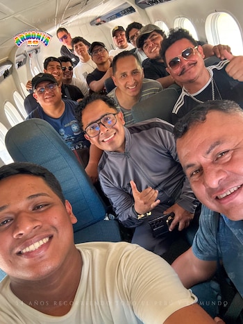 Un grupo de hombres sonríe y posa en el interior de un avión, algunos mostrando el pulgar arriba, con el logo de Armonía 10 visible