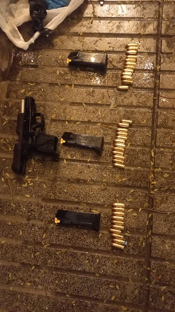 Una pistola negra, tres cargadores y decenas de balas alineadas sobre un piso de baldosas mojadas con hojas secas