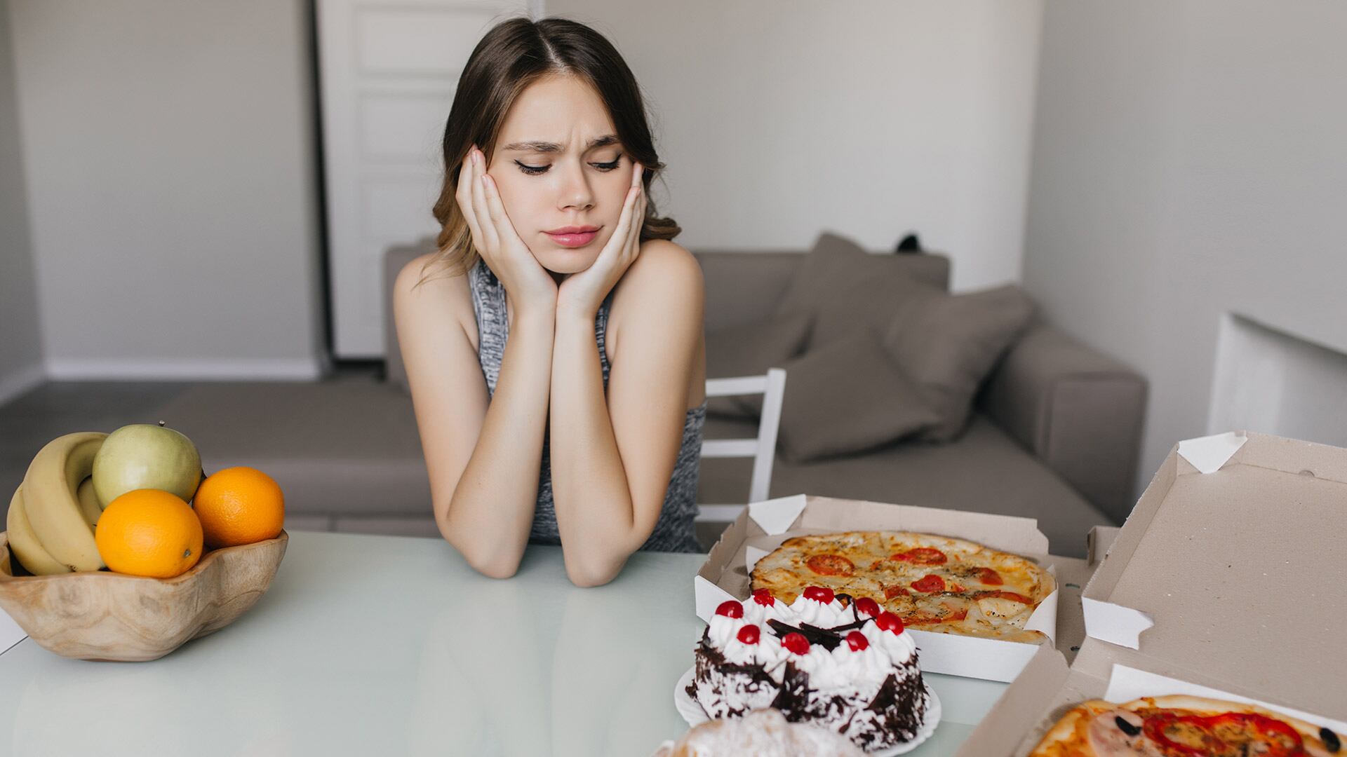 Joven decidiendo entre fruta y comida menos saludable. (Freepik)