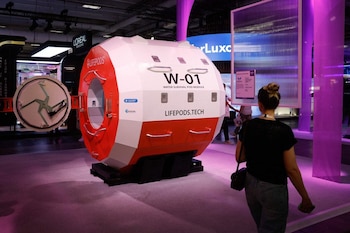 Módulo de supervivencia Lifepods W-01 blanco y rojo con puerta abierta, expuesto en un salón con luces púrpuras