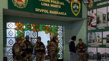 Agentes con uniforme de camuflaje y chaleco táctico frente a una entrada decorada con globos verdes y amarillos bajo letreros policiales.
