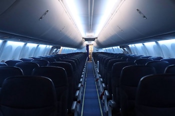 Interior de la cabina de un avión con filas de asientos de color azul oscuro, pasillo central, luces superiores y letrero de salida de emergencia