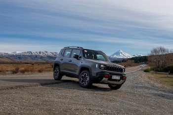 Automóvil SUV de color gris estacionado en un camino de ripio junto a una carretera, con montañas nevadas y cielo azul de fondo