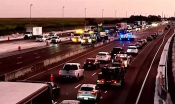 Autopista con tráfico intenso al anochecer. Grúas y vehículos de emergencia con luces parpadeantes en los carriles centrales causan atasco masivo
