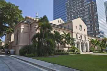 Edificio de la First Miami Presbyterian Church con cruz en el tejado, rodeada de palmeras y césped, junto a un rascacielos moderno de cristal