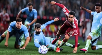 Un futbolista con uniforme rojo avanza con la pelota rodeado por tres futbolistas con uniforme celeste en una cancha de césped