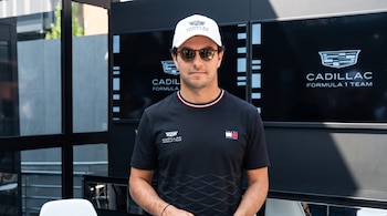 Sergio Pérez con gafas de sol, gorra blanca y camiseta negra con logotipos de Cadillac Formula 1 Team frente a pantallas con el mismo emblema.