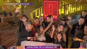 Shirley Arica, con banda "Reina de los realities", levanta los brazos sonriente, rodeada de un grupo de personas celebrando en un escenario con luces, heno y confeti