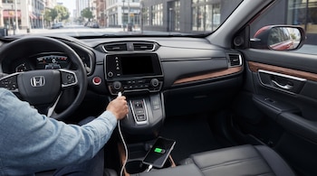Interior de un automóvil con volante, salpicadero, mano conectando cable USB a consola central y teléfono móvil cargándose en portavasos.