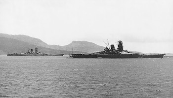 Fotografía en blanco y negro de dos grandes acorazados de la clase Yamato flotando en el agua, con montañas bajas y un cielo claro de fondo
