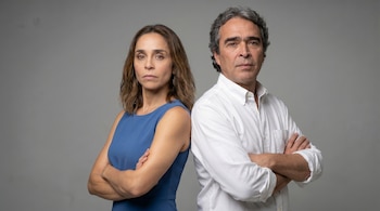Retrato de Diana Ángel (vestido azul) y Sergio Fajardo (camisa blanca), de pie y de espaldas, con brazos cruzados y expresiones serias.