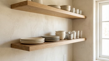 Primer plano de dos estantes flotantes de madera clara sobre una pared color crema. Los estantes exhiben platos, cuencos y vasos de tonos neutros.