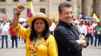 Aida Quilcué, con una camisa amarilla, sombrero de paja y puño levantado, posa junto a Hernán Orjuela, de camisa negra, brazos cruzados y sonriendo.