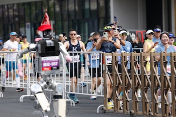 Corredores toman fotos de un robot humanoide en la II Media Maratón y Media Maratón de Robots Humaoides Beijing E-Town en Beijing, el domingo 19 de abril de 2026. (Haruna Furuhashi/Pool Foto via AP)
