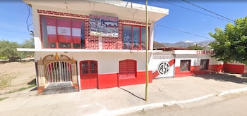 Edificio de dos plantas en blanco y rojo con cartel del Club River San Cayetano, escudo pintado en el portón y trofeos en el ventanal