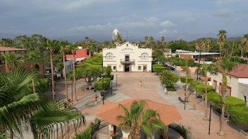Una vista aérea de la plaza principal de Loreto con un edificio blanco que dice Loreto, palmeras, un quiosco con techo de tejas, personas y montañas de fondo
