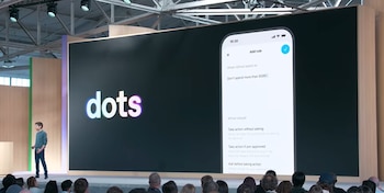 Un hombre sobre un escenario junto a una pantalla con la palabra dots y la imagen de una aplicación móvil