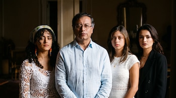 Gustavo Petro al centro vistiendo camisa azul clara junto a tres mujeres jóvenes frente a la cámara en un ambiente interior oscuro.