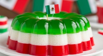 Gelatina redonda en capas verde, blanca y roja, imitando la bandera de México, con una pequeña bandera mexicana como adorno en la parte superior.