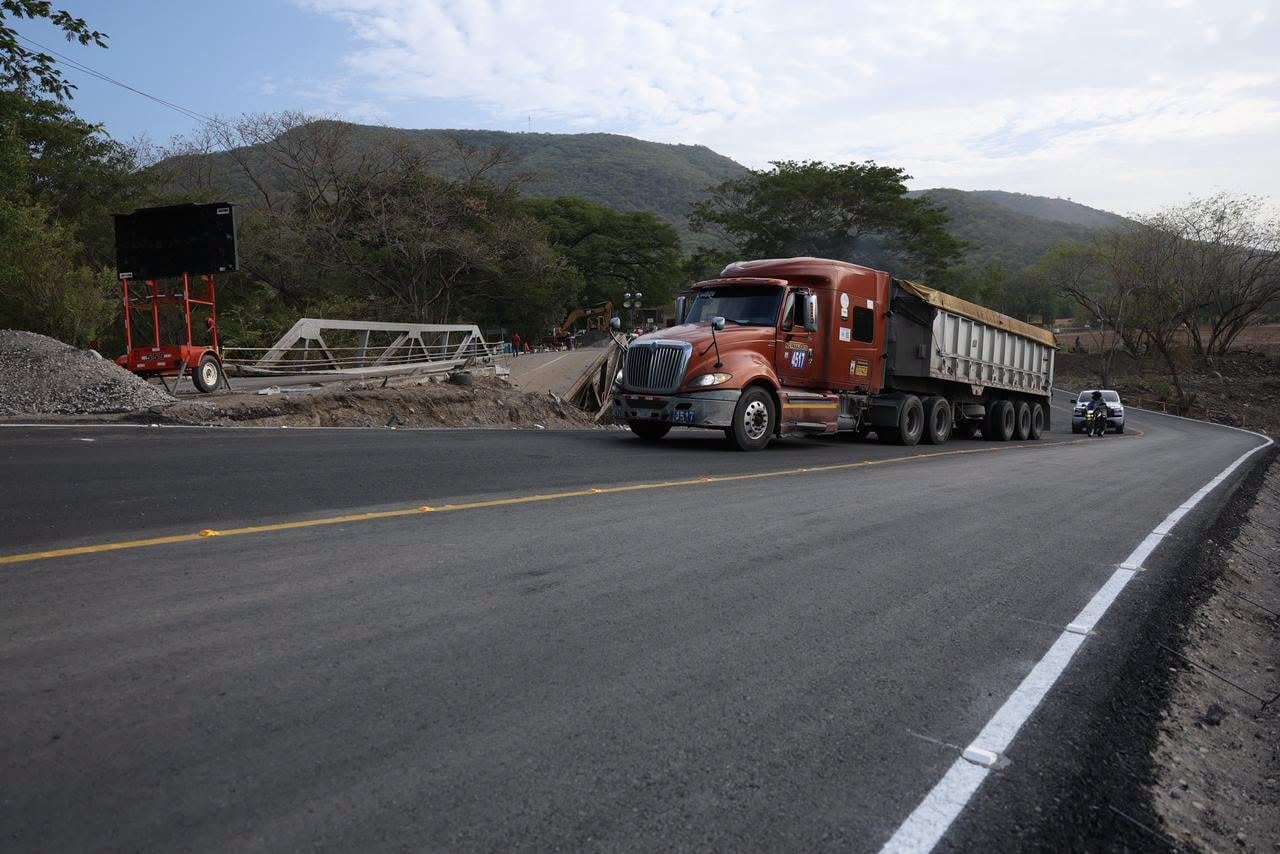 Un camión de carga transita por una carretera recién asfaltada cerca de un puente en construcción y zonas montañosas. (Ministerio de Comunicaciones, Infraestructura y Vivienda)