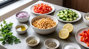 Garbanzos, tomates, pepinos, cebolla roja, aceite de oliva, perejil, limones, orégano, pimienta negra, sal y pimiento rojo en recipientes.