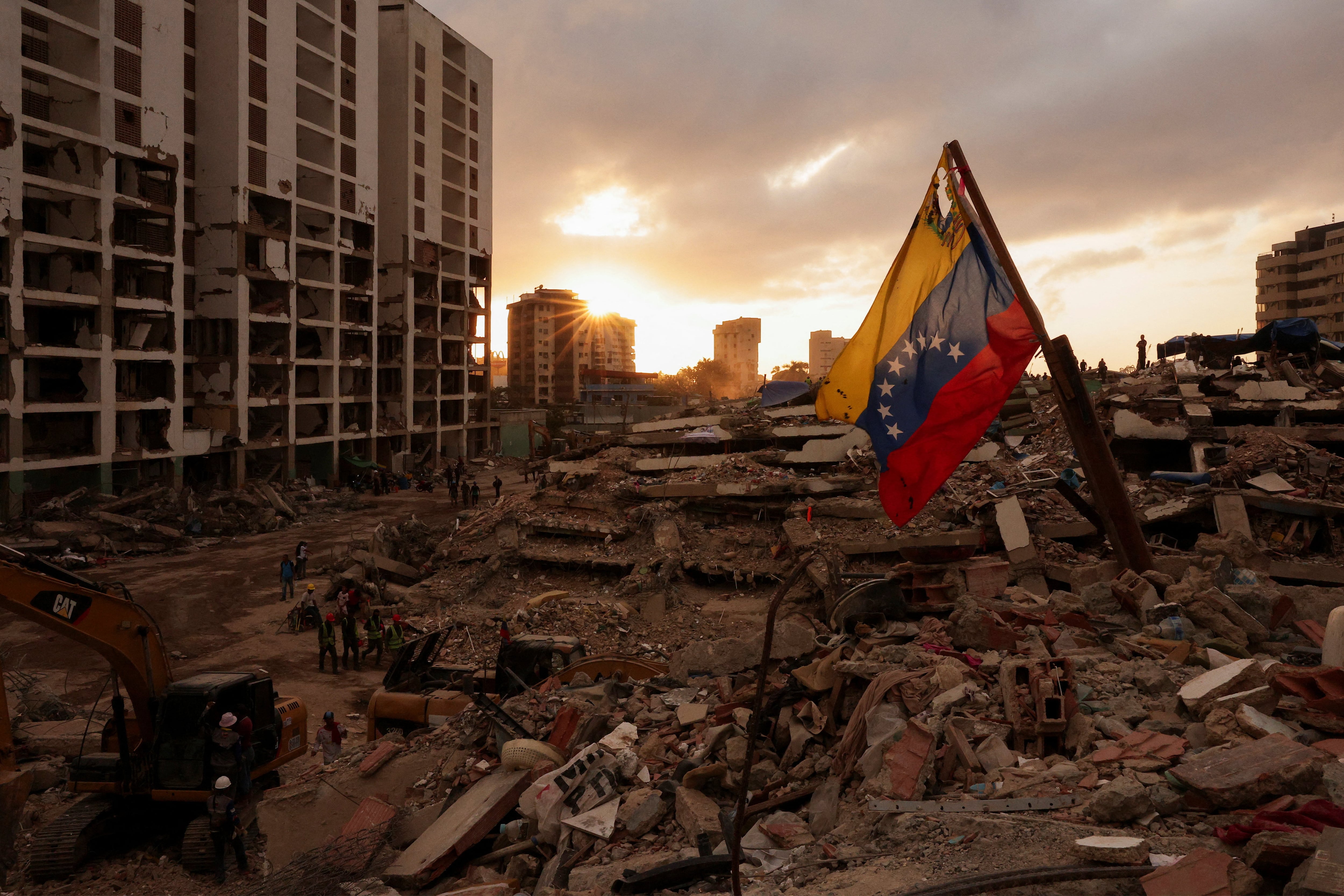 Una bandera venezolana ondea mientras la gente busca los cuerpos de sus seres queridos entre los escombros, tras los terremotos que sacudieron Venezuela el 24 de junio y que causaron la muerte y el desplazamiento de miles de personas, en Caraballeda, La Guaira (REUTERS/Gaby Oraa)