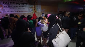 Grupo de mujeres en un interior con iluminación tenue. Varias de espaldas o cubriendo sus rostros. Un cartel en la pared indica 'NO SE ADMITE LA TRATA DE PERSONAS'