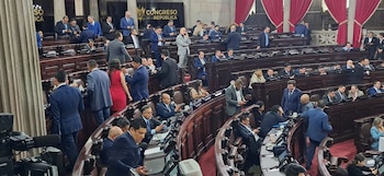 Un amplio salón con filas de escaños de madera ocupados por hombres y algunas mujeres. Se observa un cartel con el texto "Congreso de la República"