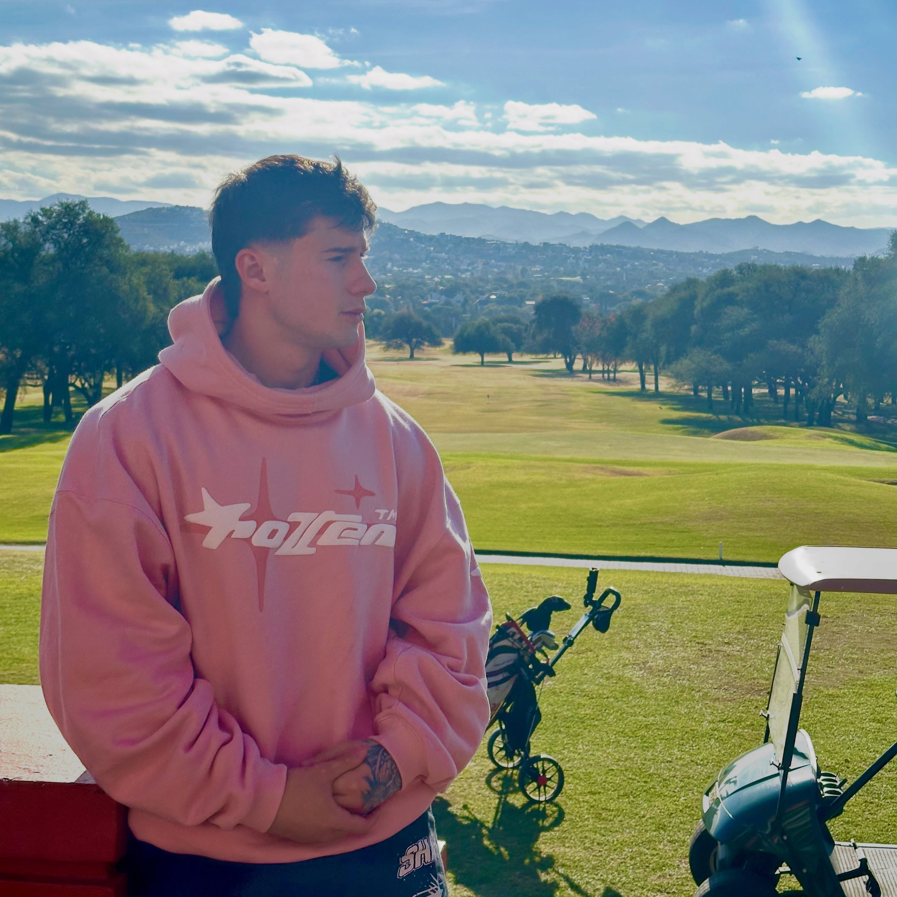 Tomás Mazza viste una sudadera rosa mientras permanece de pie en un campo de golf.