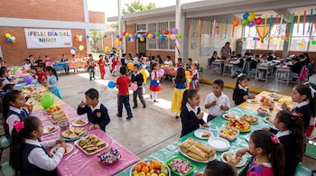Niños celebran el Día del Niño en el patio de una escuela primaria mexicana, con mesas llenas de comida, globos de colores y un letrero festivo.