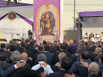 Hombres de espaldas con trajes oscuros y manos sobre los hombros frente a un estandarte con la imagen del Señor de los Milagros
