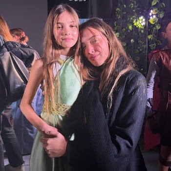 Las hijas de la modelo posan abrazadas en un ambiente con decoración de follaje verde y luces.
