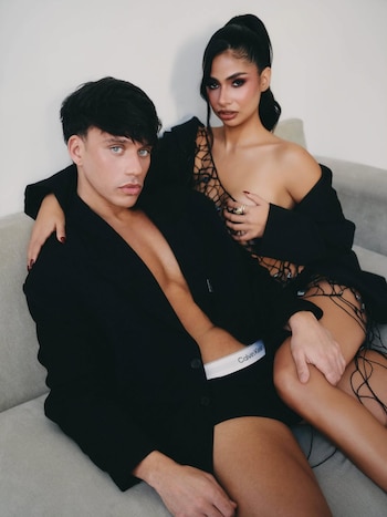 Daniela Celis y Nick Sicaro posan en un sofá. Él usa boxers Calvin Klein y blazer negro suelto, ella un blazer negro y top de red. Ambiente minimalista