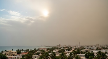 Vista panorámica de una ciudad dominicana con edificios bajos y palmeras a lo largo de la costa, bajo un cielo opaco con una densa bruma beige-grisácea.