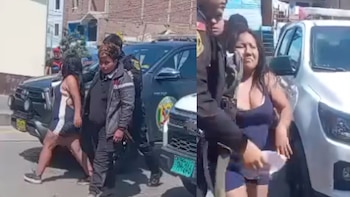 Dos mujeres son escoltadas por policías cerca de vehículos policiales blancos y negros en una calle soleada, con edificios de fondo