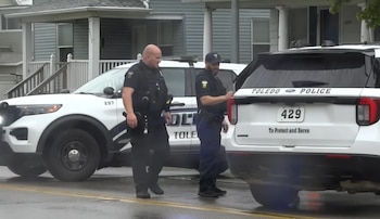 Dos agentes de policía junto a dos vehículos policiales blancos de Toledo Police en una calle frente a casas residenciales